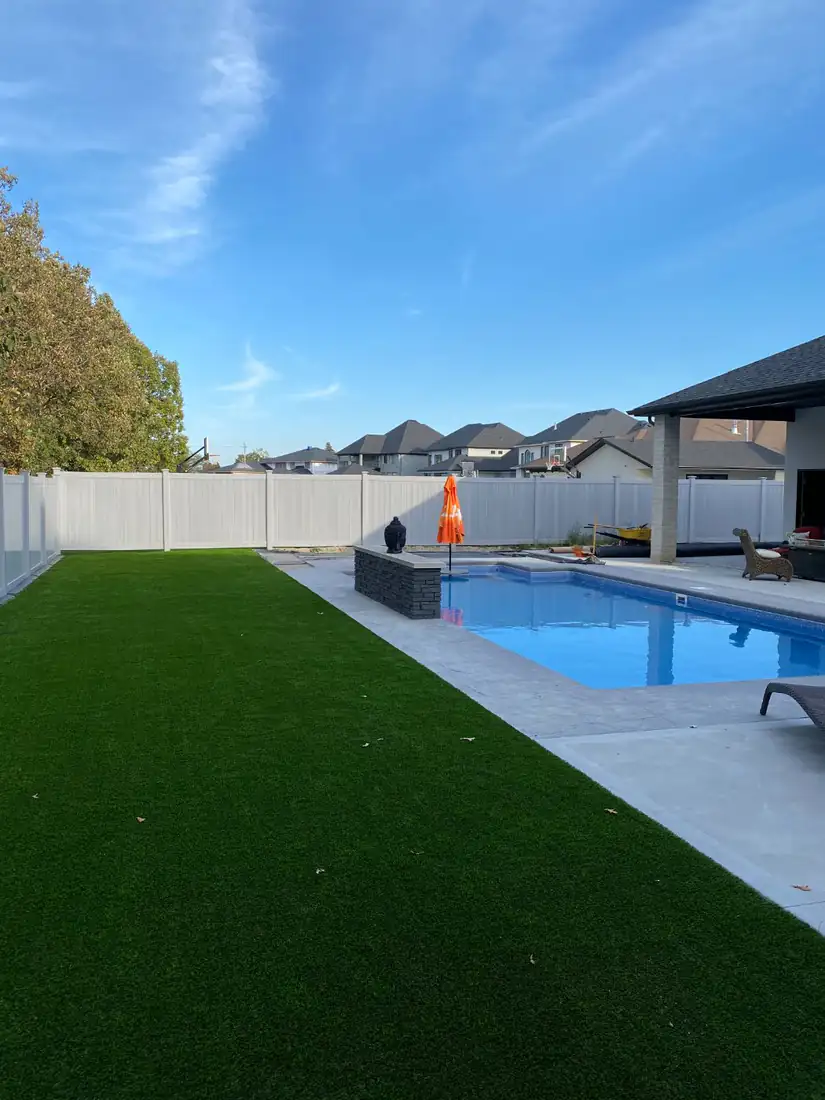 Backyard turf beside a pool and vinyl fence