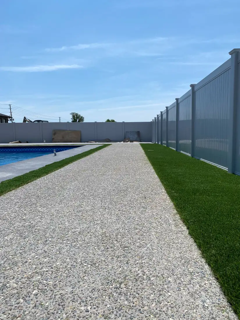 Exposed aggregate walkway between the pool and turf, along a vinyl fence